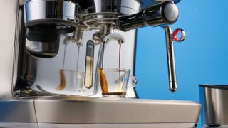 the breville oracle dual boiler / sage oracle dual boiler in stainless steel, showing its touchscreen, steam wand, built in grinder, and espresso shots