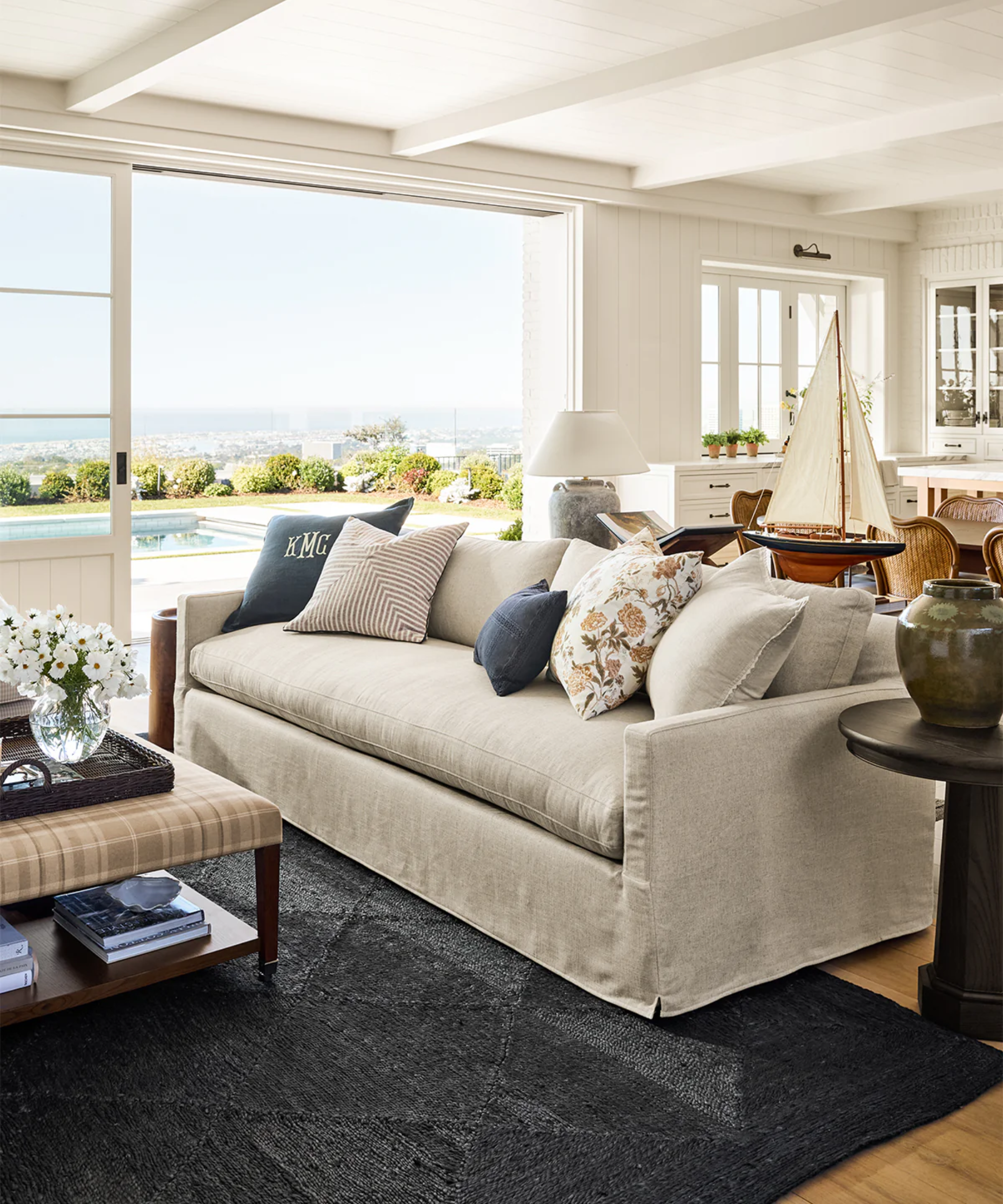 a nautical living room with a cream couch with several pillows on it, a blue textured rug, and sliding doors that open up to a pool in the backyard