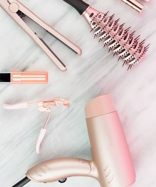 Rose gold hairbrush, straighteners, curlers, clips, and a hair dryer on a gray marble surface