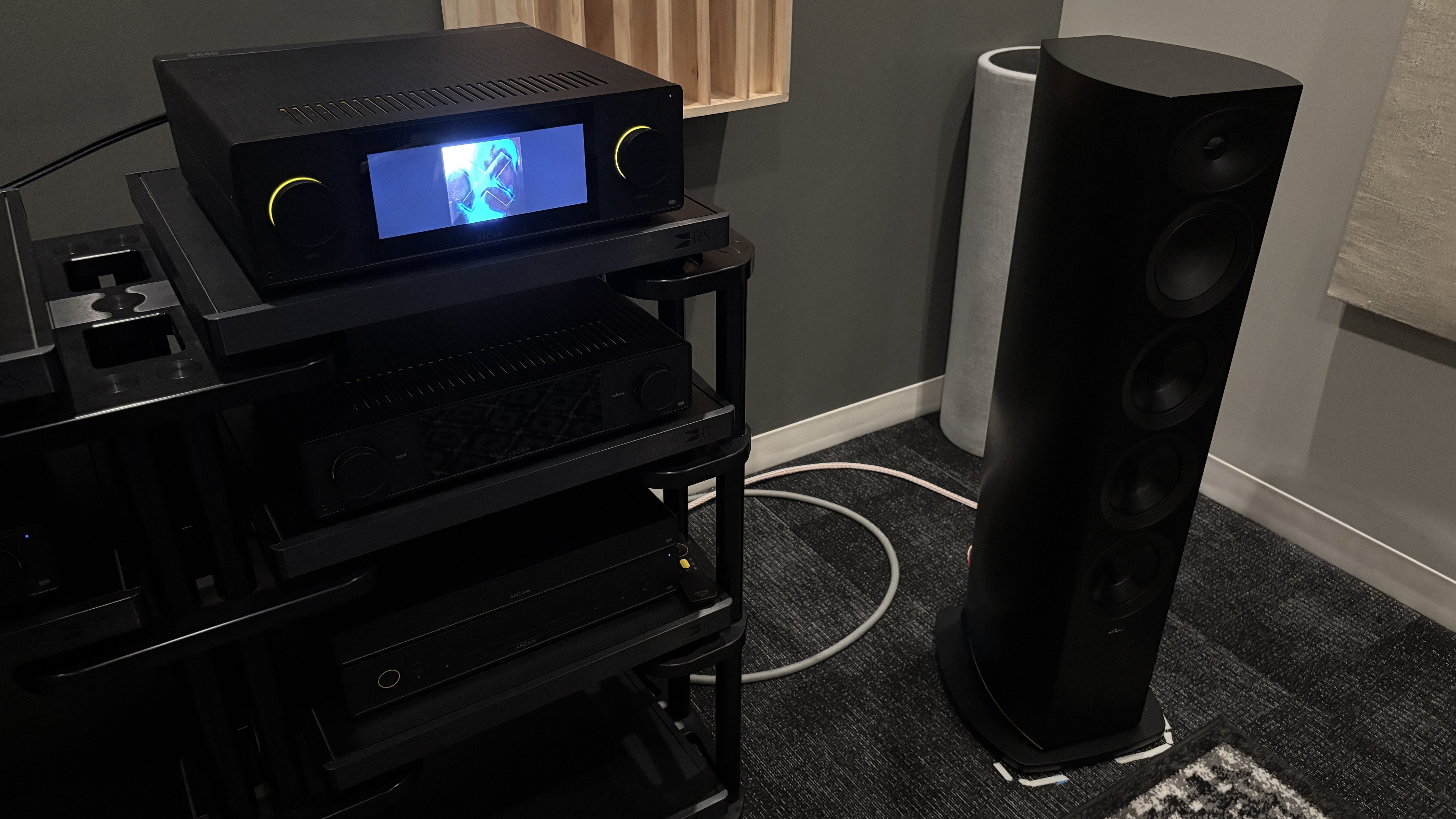 Arcam Radia R45 floorstanding speaker on the floor next to a rack with an Arcam SA45 streaming amplifier