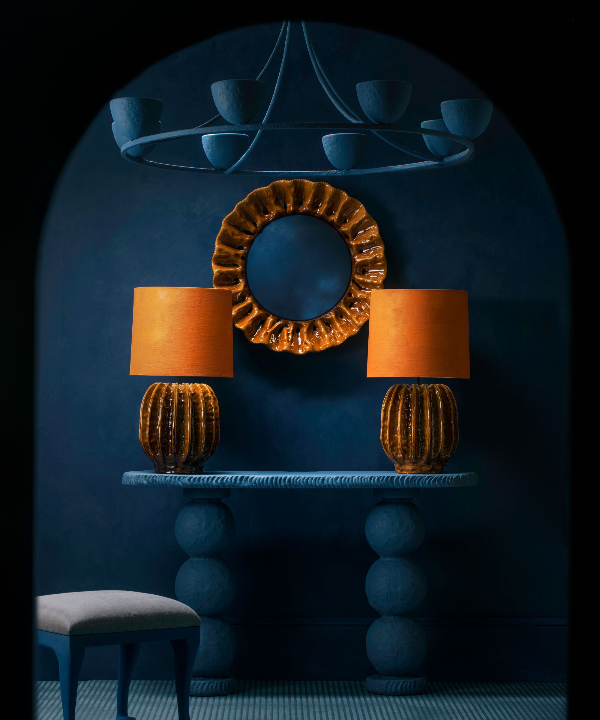 A dark navy wall with a circular resin lamp in a deep orange color and two matching table lamps