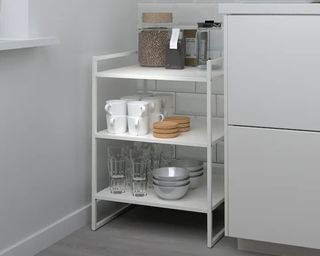 a small shelving unit full of kitchen essentials next to a kitchen counter, to show one of w&h's pan storage ideas