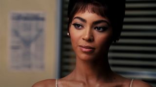 Beyoncé half smiling in a retro hairstyle and costume in Dreamgirls.