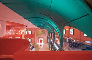 A view of the lower level of the cinema which has pink walls, a blue curved roof, bird shaped pendant light and patterned floor tiles.