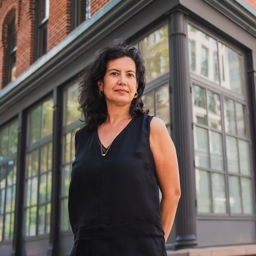 Image of a woman in a black tank and black pants standing outside a building.