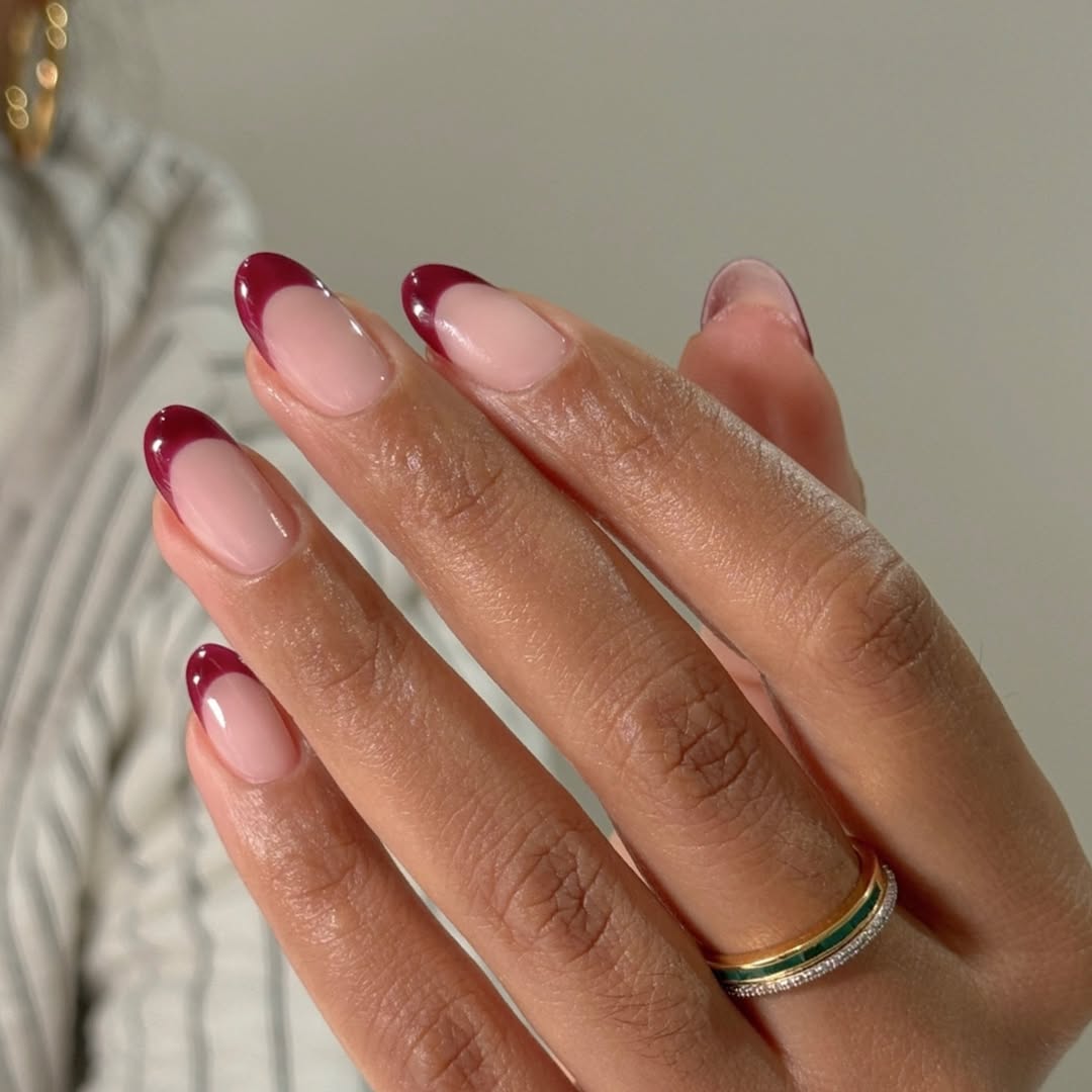 Close-up photo of a person&amp;rsquo;s hands showcasing an almond-shaped nail manicure featuring burgundy tips.