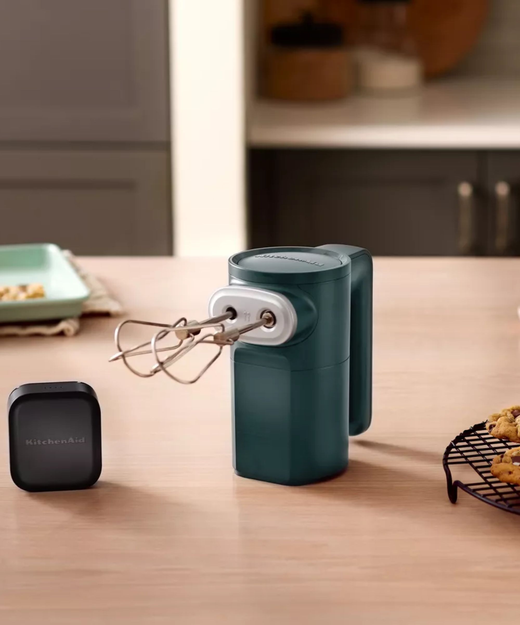 Green KitchenAid hand mixer on wooden countertop with a black battery pack beside it