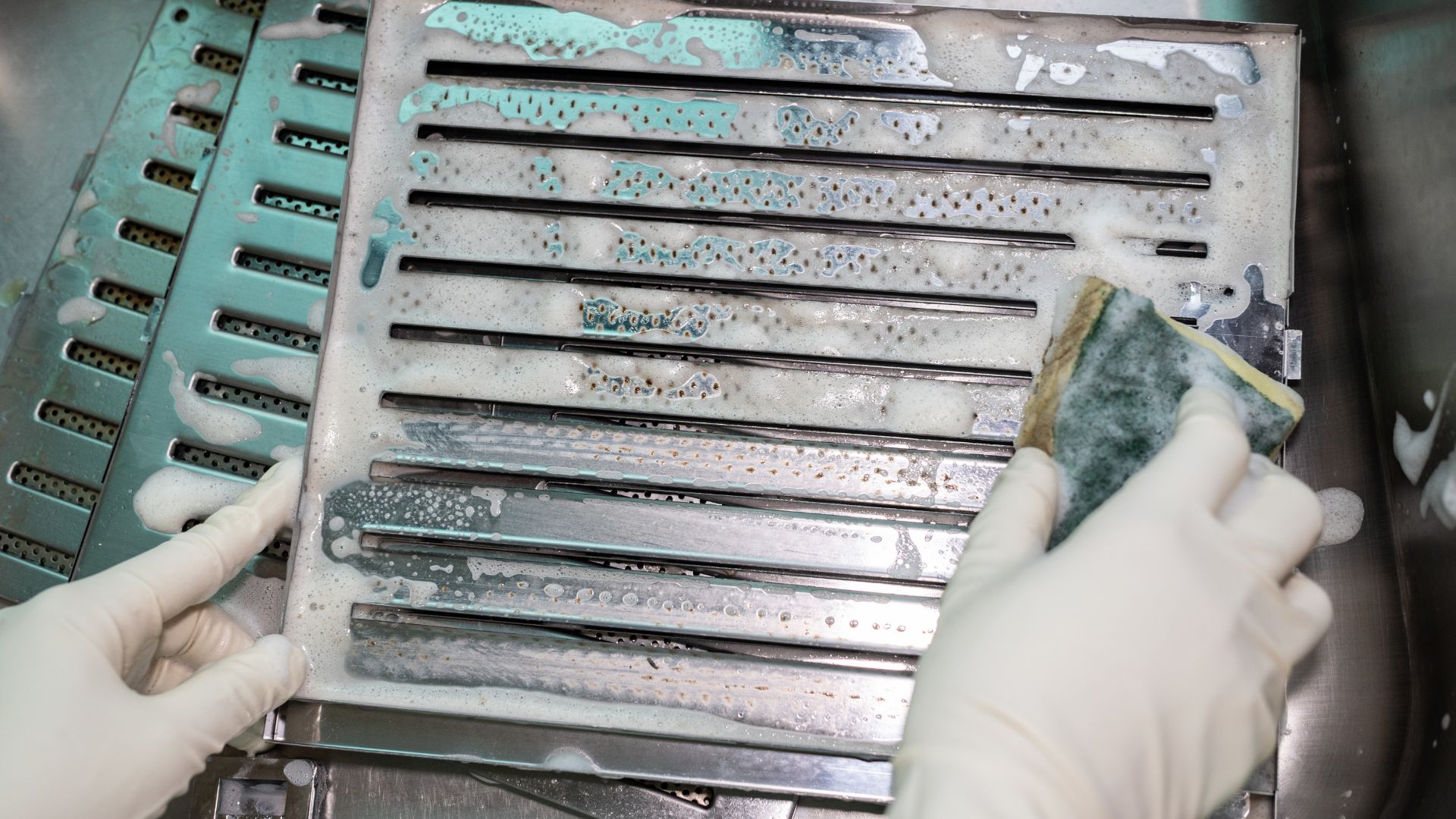 picture of someone scrubbing extractor fan filters in sink with scourer sponge