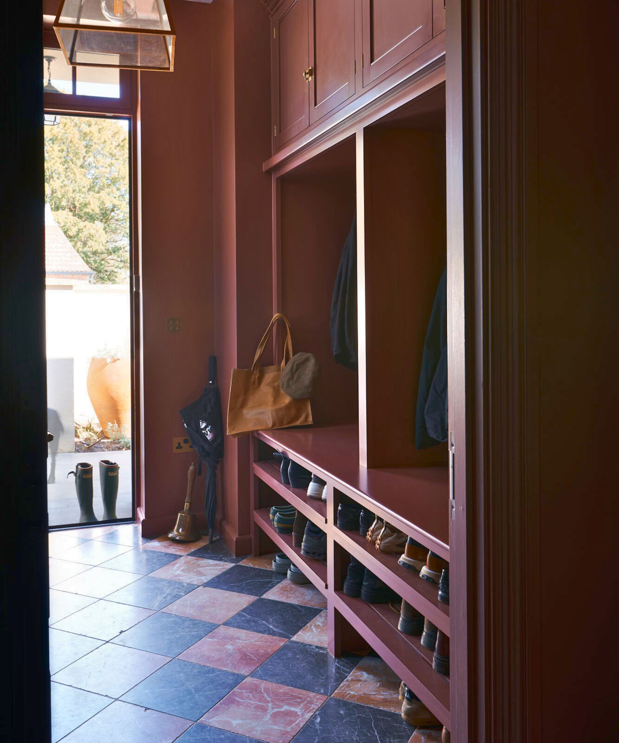 Moody burgundy boot room with marble checkered floor and built-in storage to the right, showing shoes on the lower third, vertical open cubbies for coats, and closed cabinets at the tome
