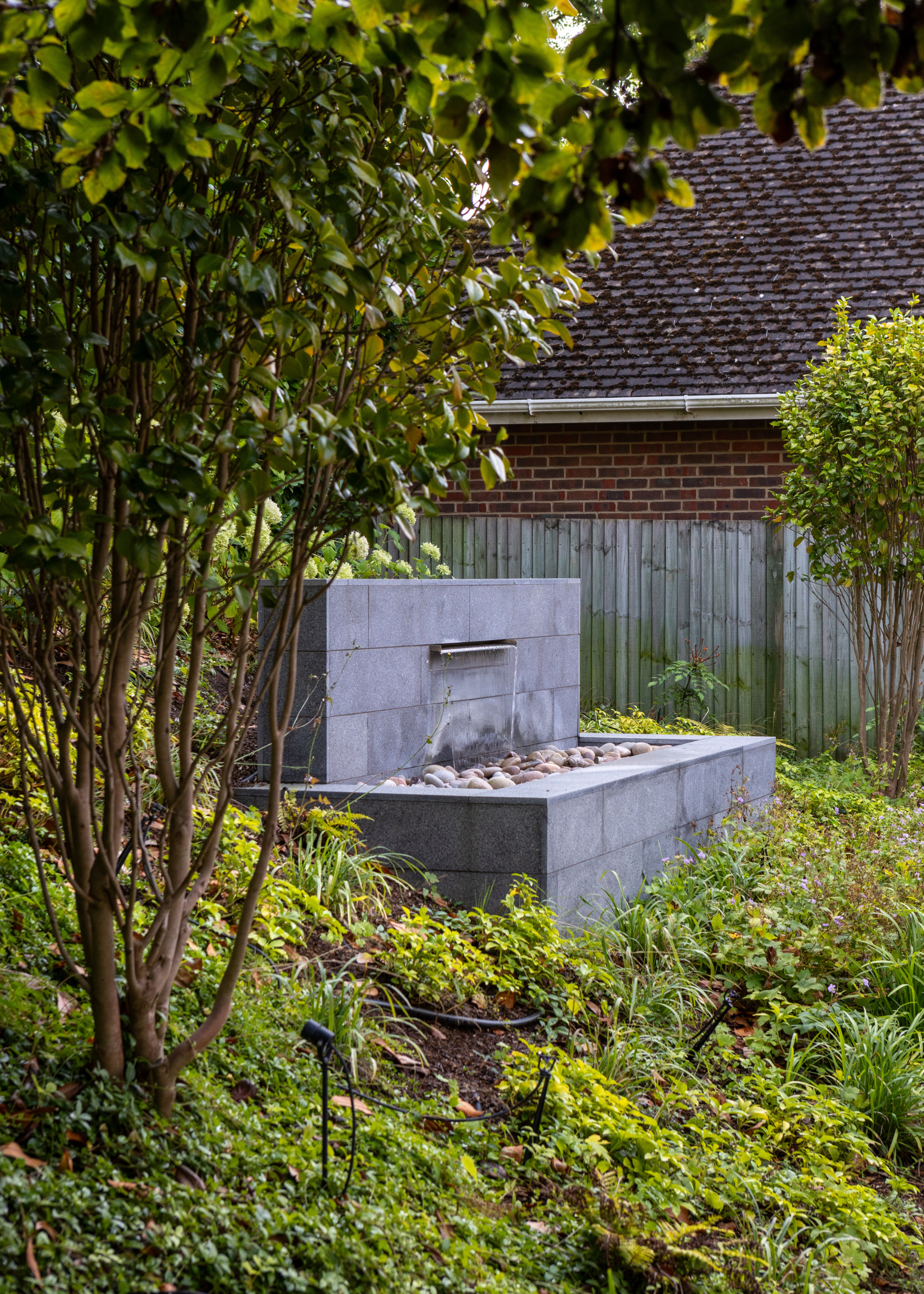 a wider water fountain falling on rocks near the hedge of a garden