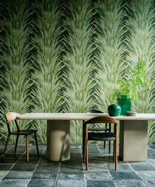 Dining room with green, botanical leaf print wallpaper, rectangular, concrete-style dining table, wooden dining chairs with black leather seats, table decorated with green vases and ornaments, traditional stone gray flooring