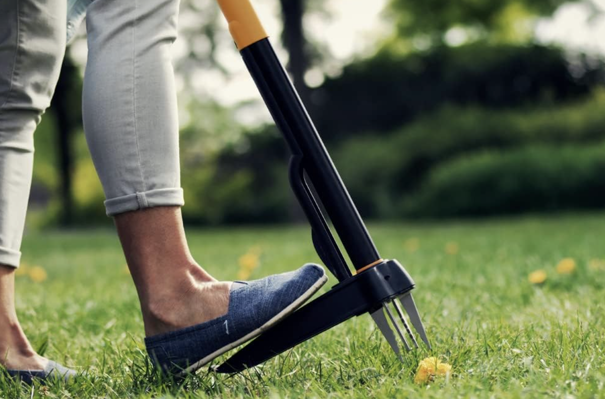 A woman steps down onto a long handled weed removing tool 