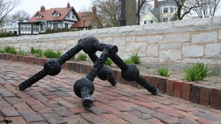 A black ball and socket robot walks on four limbs down a brick path with houses in the background