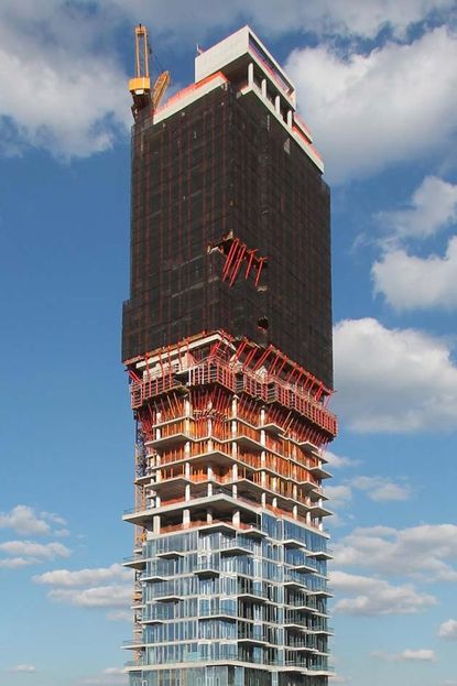 High-rise residential tower in New York, 56 Leonard, multiple windows, red metal frames, and black cladding to th etop , yellow crane and white viewing section on the top, blue cloudy sky