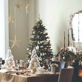 A dining room with the table set and a Christmas tree with golden decorations in the background