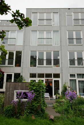 Exterior view of the flat, featuring grey concrete with vertical lines, balconies with clear glass white french doors.
