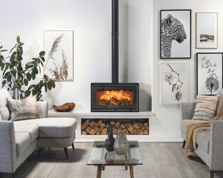 Free-standing stove with logs stored beneath surround in white with art on the walls and greige flooring