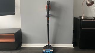 The Shark Anti Hair Wrap Cordless Stick Vacuum Cleaner with PowerFins & Flexology in stick vacuum mode resting against a grey wall