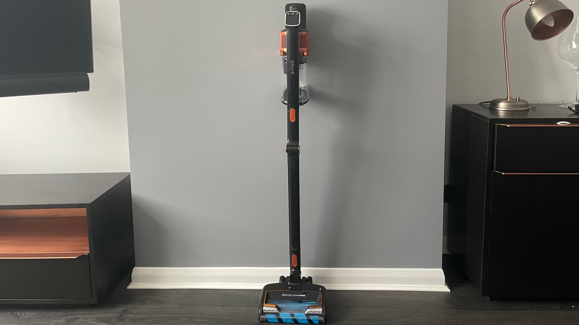 The Shark Anti Hair Wrap Cordless Stick Vacuum Cleaner with PowerFins & Flexology  in stick vacuum mode resting against a grey wall