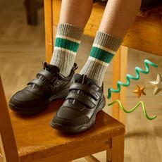Kid with shoes on a wooden scholl chair wearing black velcro school trainers sold at Clarks