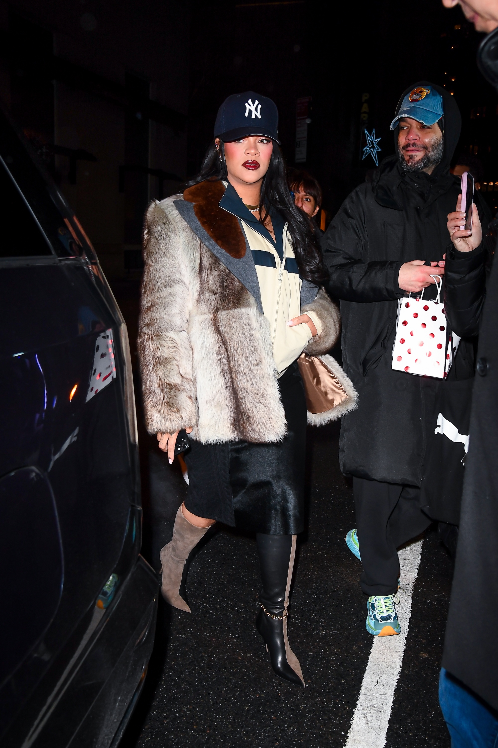 Rihanna in Manhattan on January 17, 2026 wearing a Prada fur coat, Loewe two tone boots, a black skirt, a casual track jacket, and a baseball cap