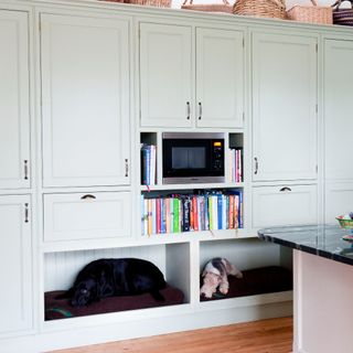 A kitchen with built-in cabinets and joinery in a dove grey shade with a built-in microwave and dog beds