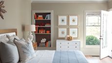 Coastal bedroom with Pashmina by Benjamin Moore walls, a bed with pale blue and white bedding, a wall of nautical prints, a white dresser, and built-in bookshelves with orange boxes.