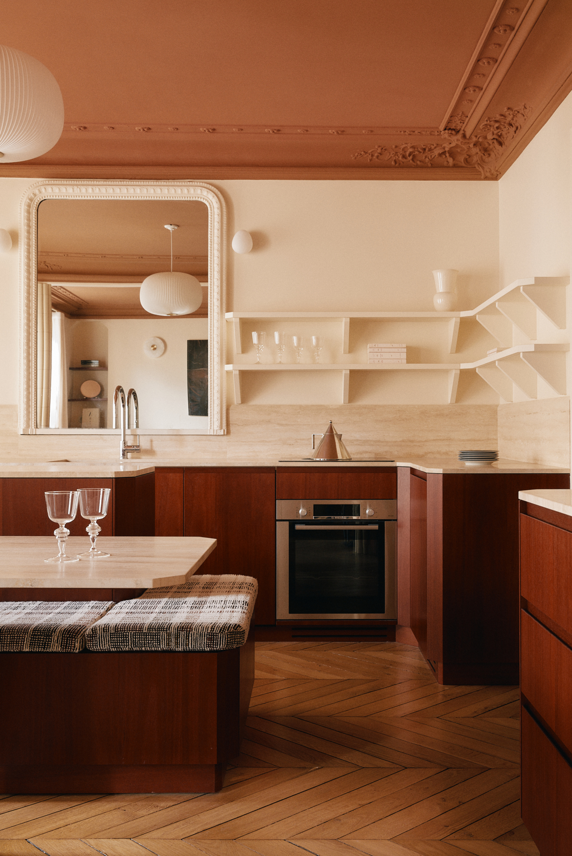 Image of a kitchen with cream walls and ceilings that are painted in a dark burnt orange/terracotta. The cabinet is a warm red wood that looks almost color blocked against the white walls.