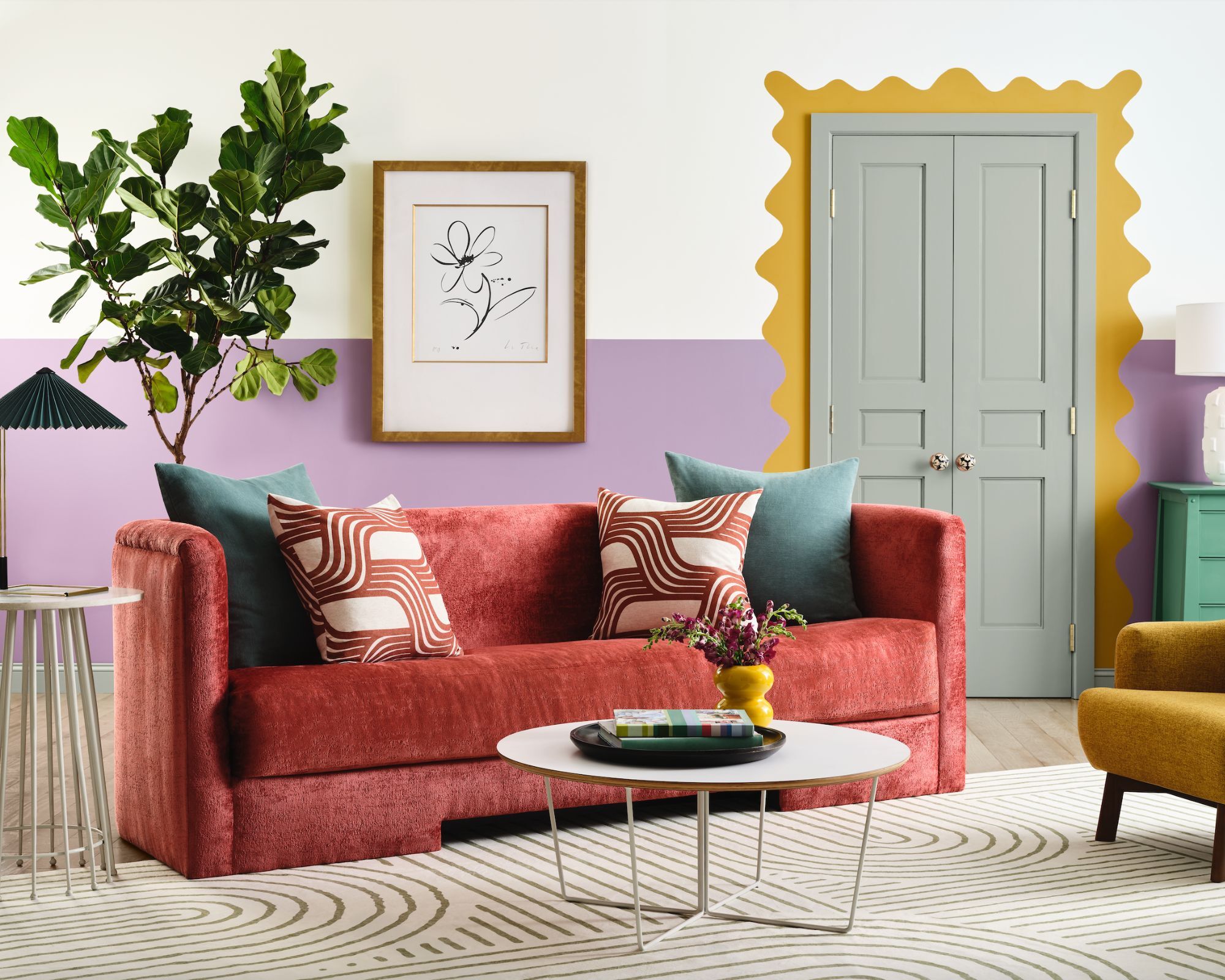 A living room with a wall painted half in white, half in purple with a yellow scalloped door frame and a red sofa
