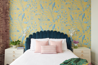 A bedroom with a yellow wallpaper, and teal headboard