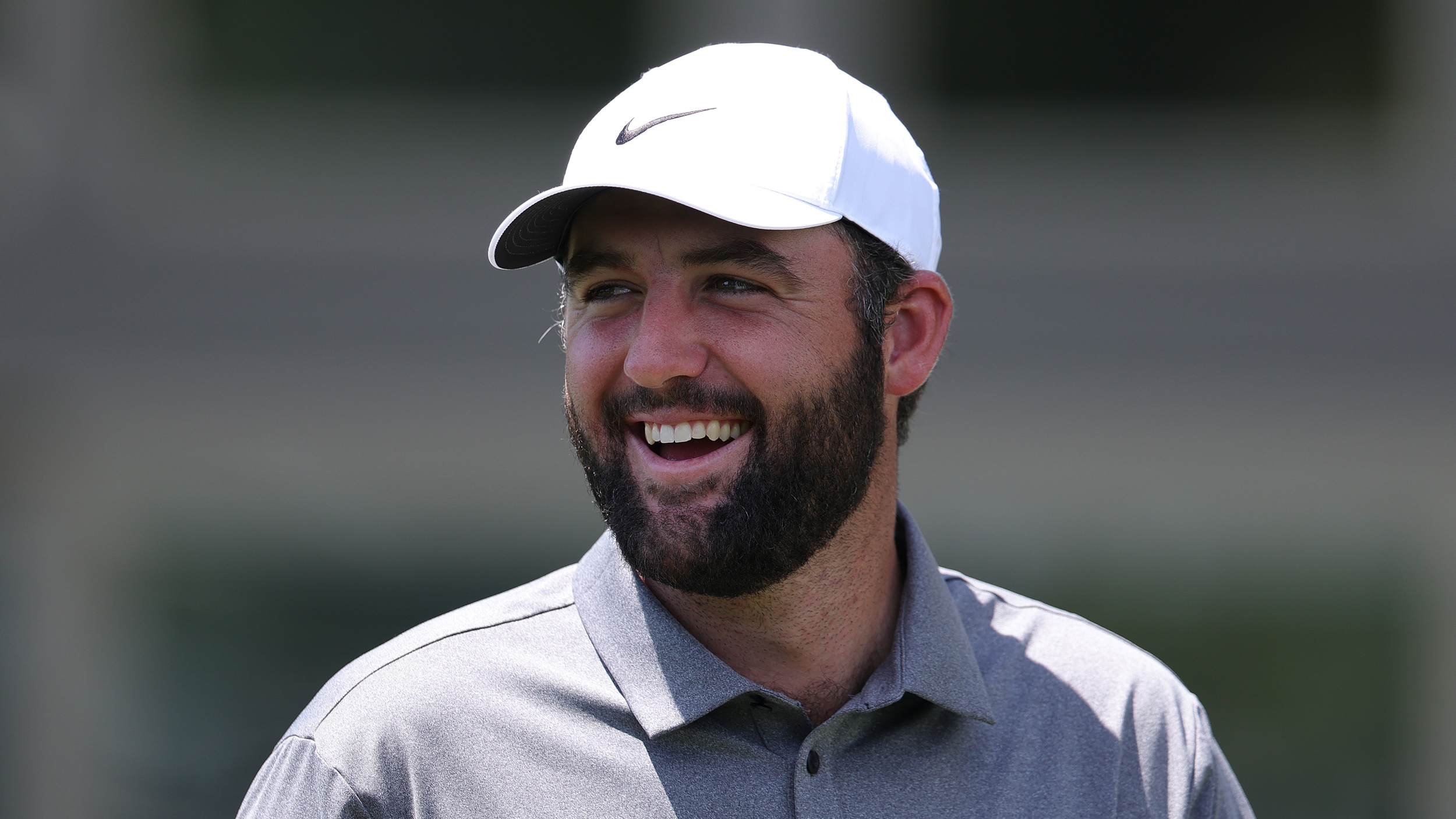 Scottie Scheffler smiles in a white Nike cap and grey polo