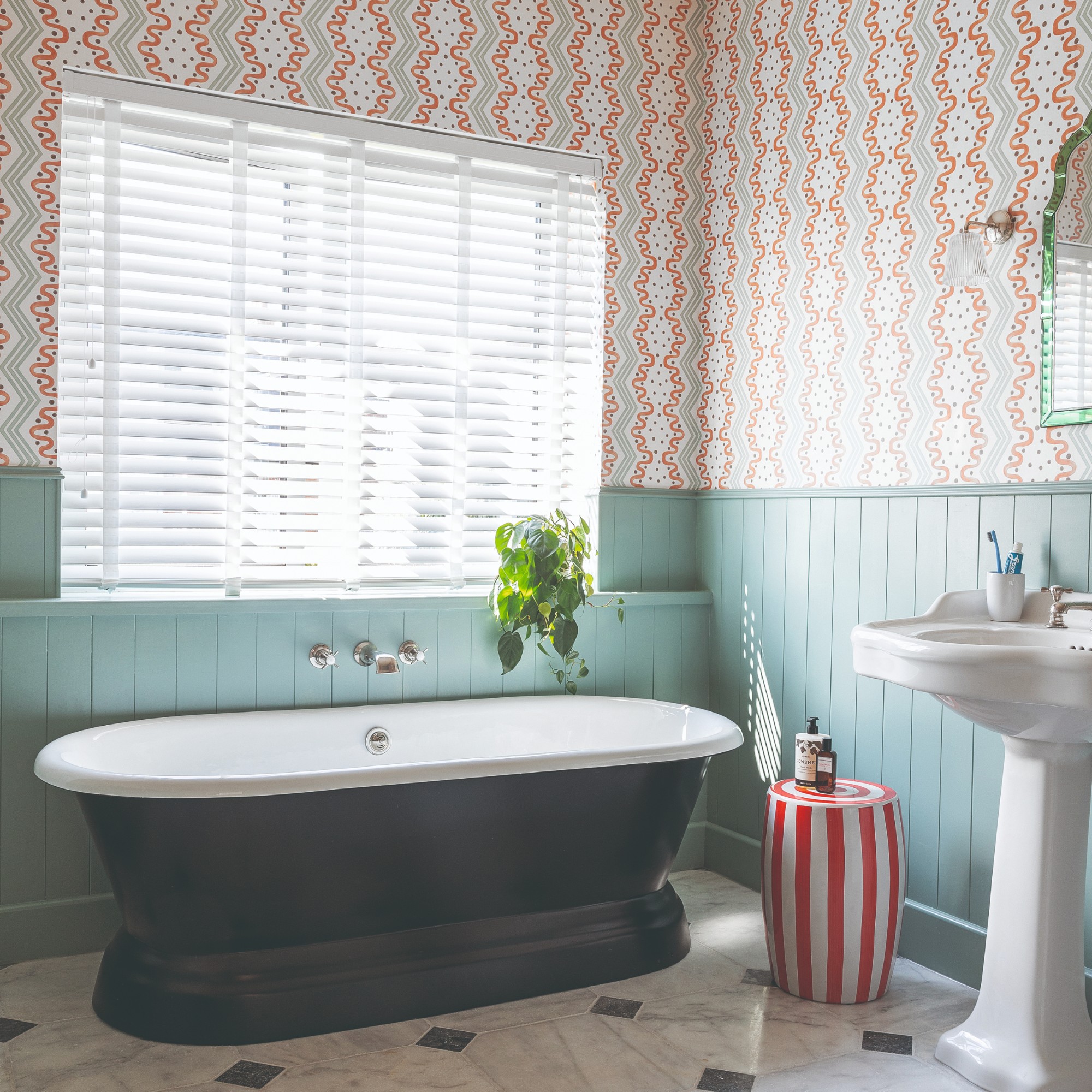 A bathroom with half-height tongue and groove panelling in turquoise and patterned wallpaper on the upper half of the wall