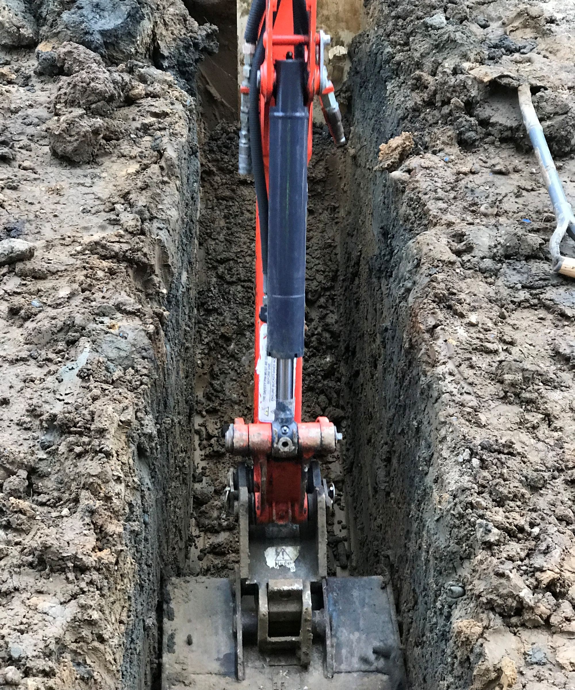 The arm of a red digger digging a trench for drainage