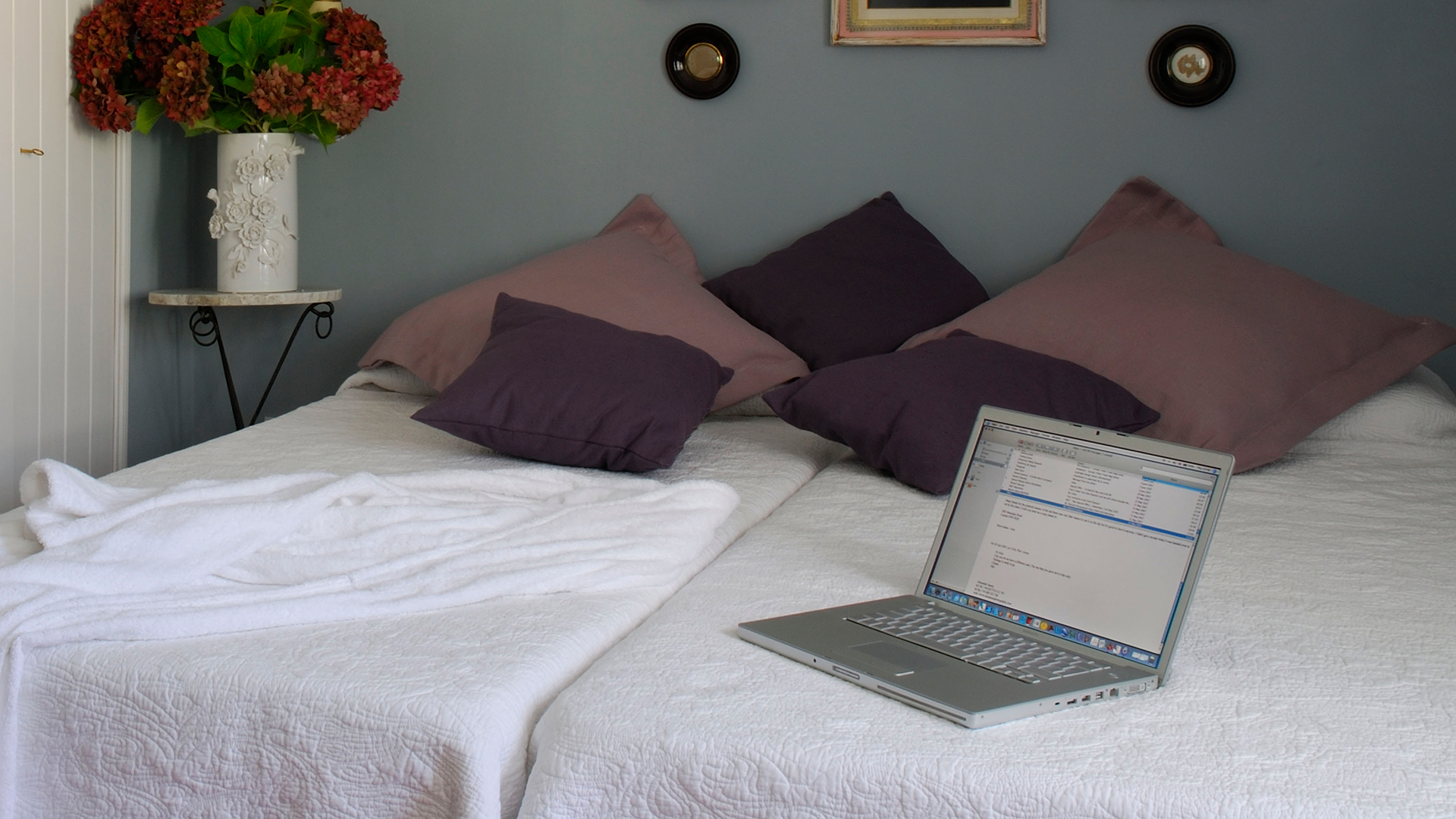 Bed with laptop in a blue room with layered purple scatter cushions