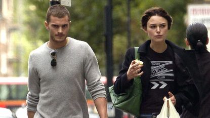 Jamie Dornan and Keira Knightley walk along a street with shopping bags.