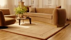 Beige mid-century-inspired Serge Bordered rug from Nate Berkus's 2026 Rugs USA collaboration lining the floor of a warm Manhattan living room styled with soft-lined contemporary furniture