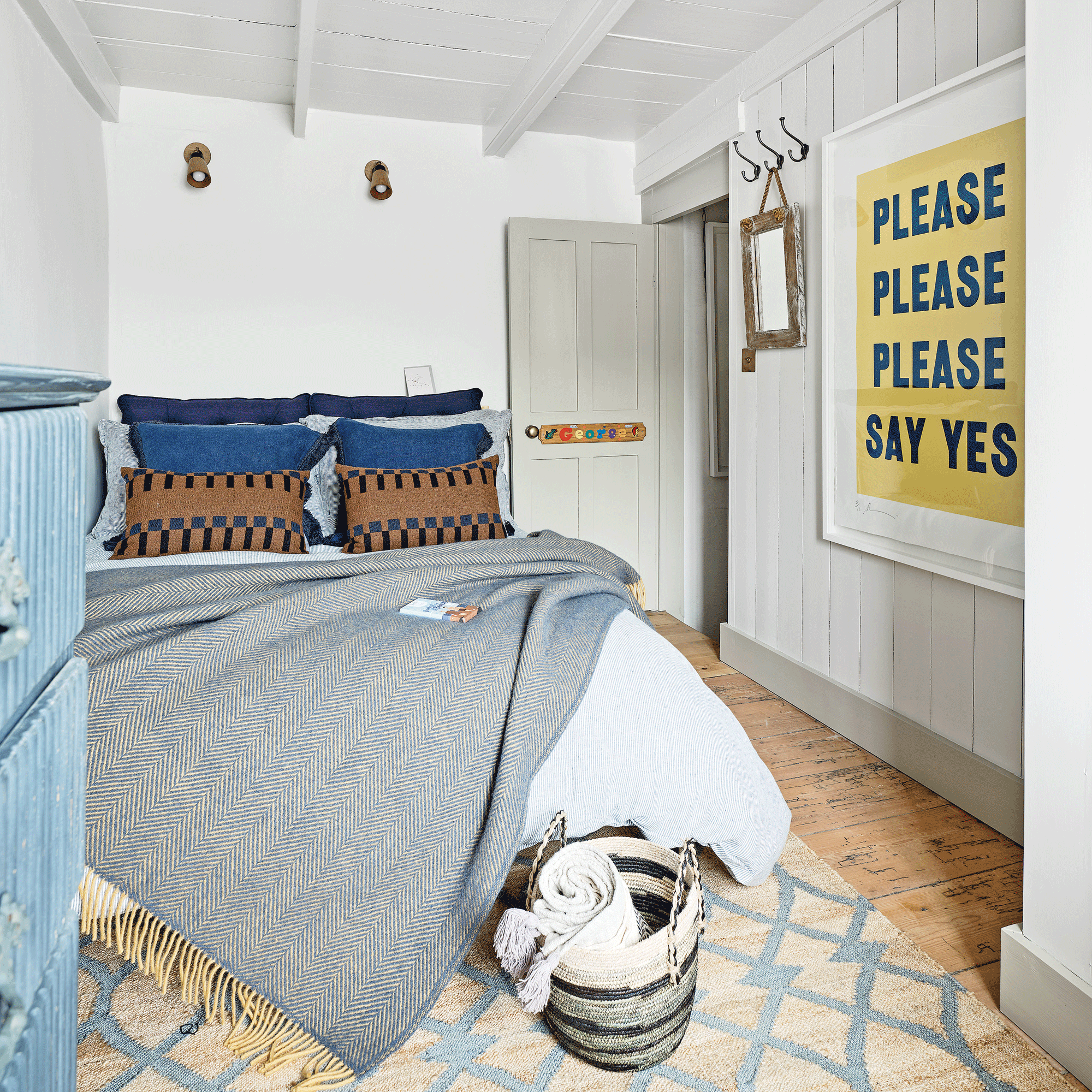 a bedroom with white walls and panelling with layers of bedding in various shades