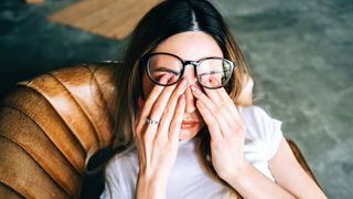 Young woman rubs her eyes after using glasses. Eye pain or fatigue concept