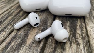 One earbud each from the Apple AirPods Pro 2 and AirPods 4 lying side by side at an angle on a wooden surface.