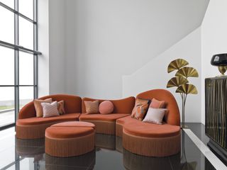 A curved orange sofa with fringing detail and soft pink cushions