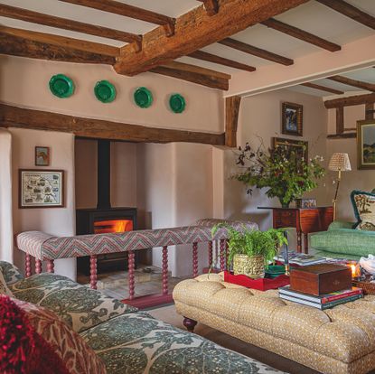 sitting room in English farmhouse with beamed ceiling, pink walls, large fireplace and upholstered furniture