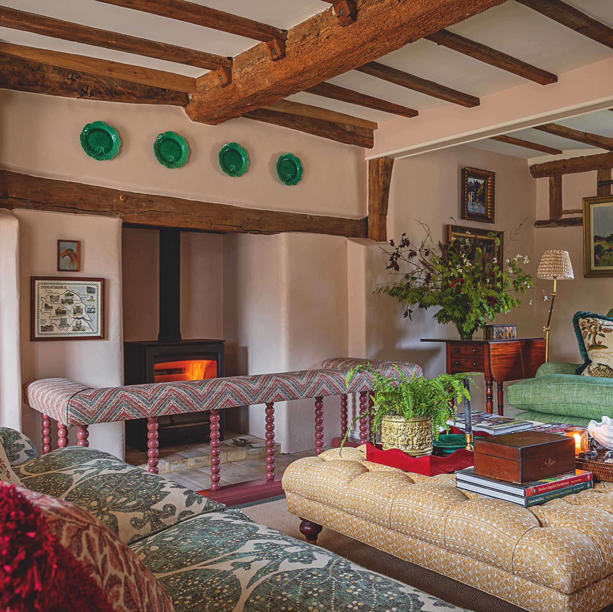 sitting room in English farmhouse with beamed ceiling, pink walls, large fireplace and upholstered furniture