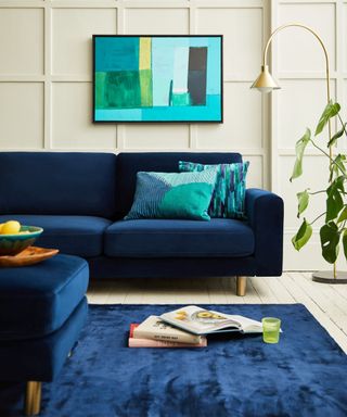 A living room with cream panelled walls and a blue navy velvet Snug sofa and rug.