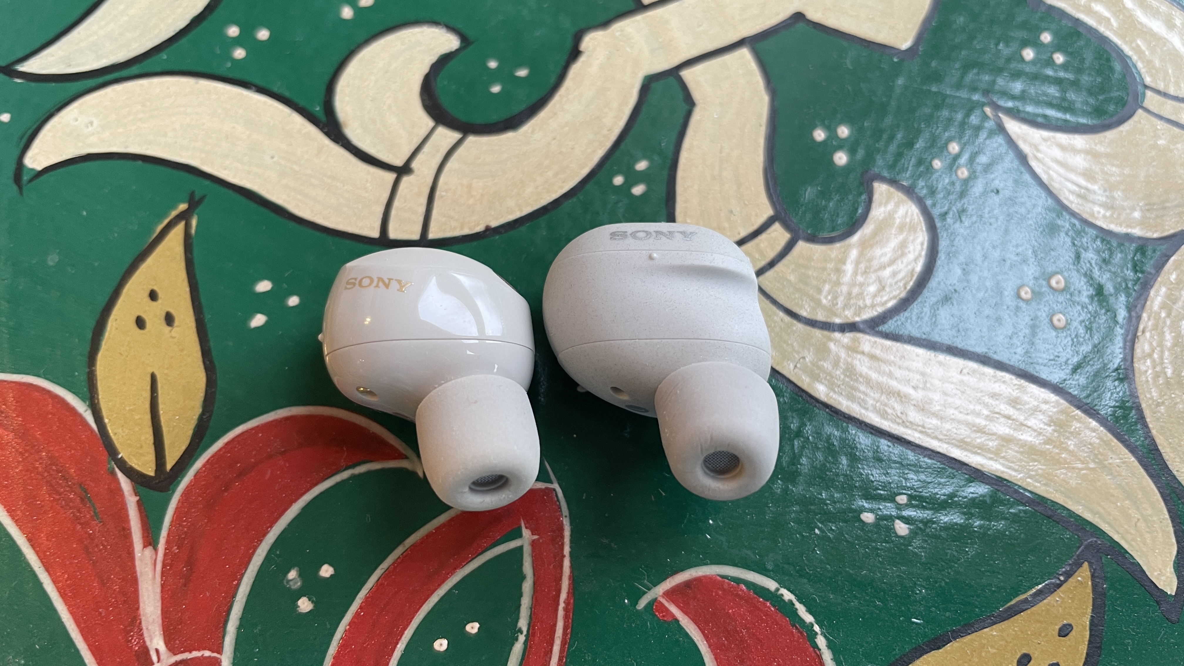 Sony WF-1000XM6 earbuds next to the older-gen. WF-1000XM5 and WF-C710N, on colorful table