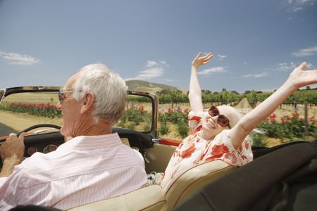 A retired couple looks joyful as they drive with the top down in the countryside.