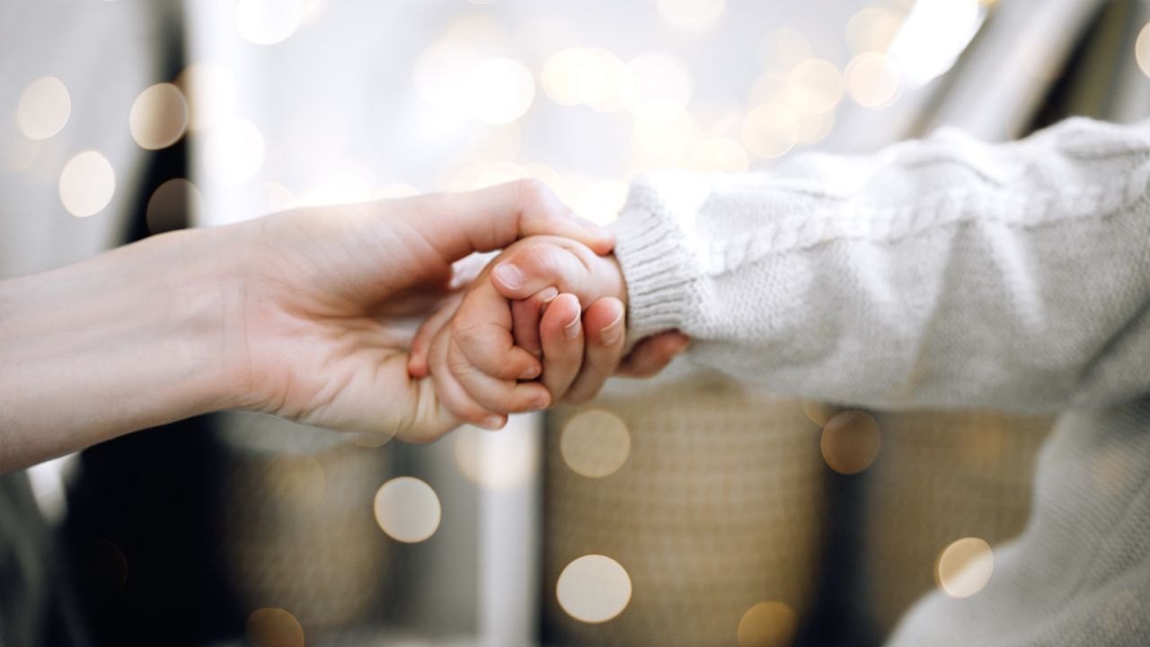 An adult holds the hand of a toddler in a loving, caring way.