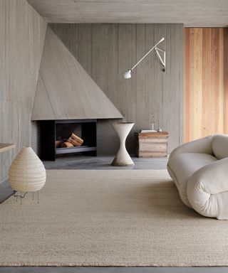 Living room with concrete-effect walls, curvaceous sofa, large textured neutral rug and fireplace