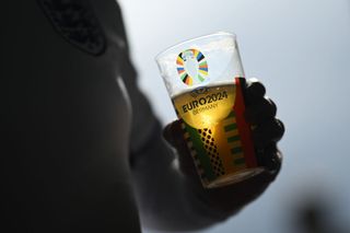 A detailed view of a UEFA EURO 2024 branded cup with a pint of beer in it, held by a fan of England, prior to the UEFA EURO 2024 group stage match between Serbia and England at Arena AufSchalke on June 16, 2024 in Gelsenkirchen, Germany