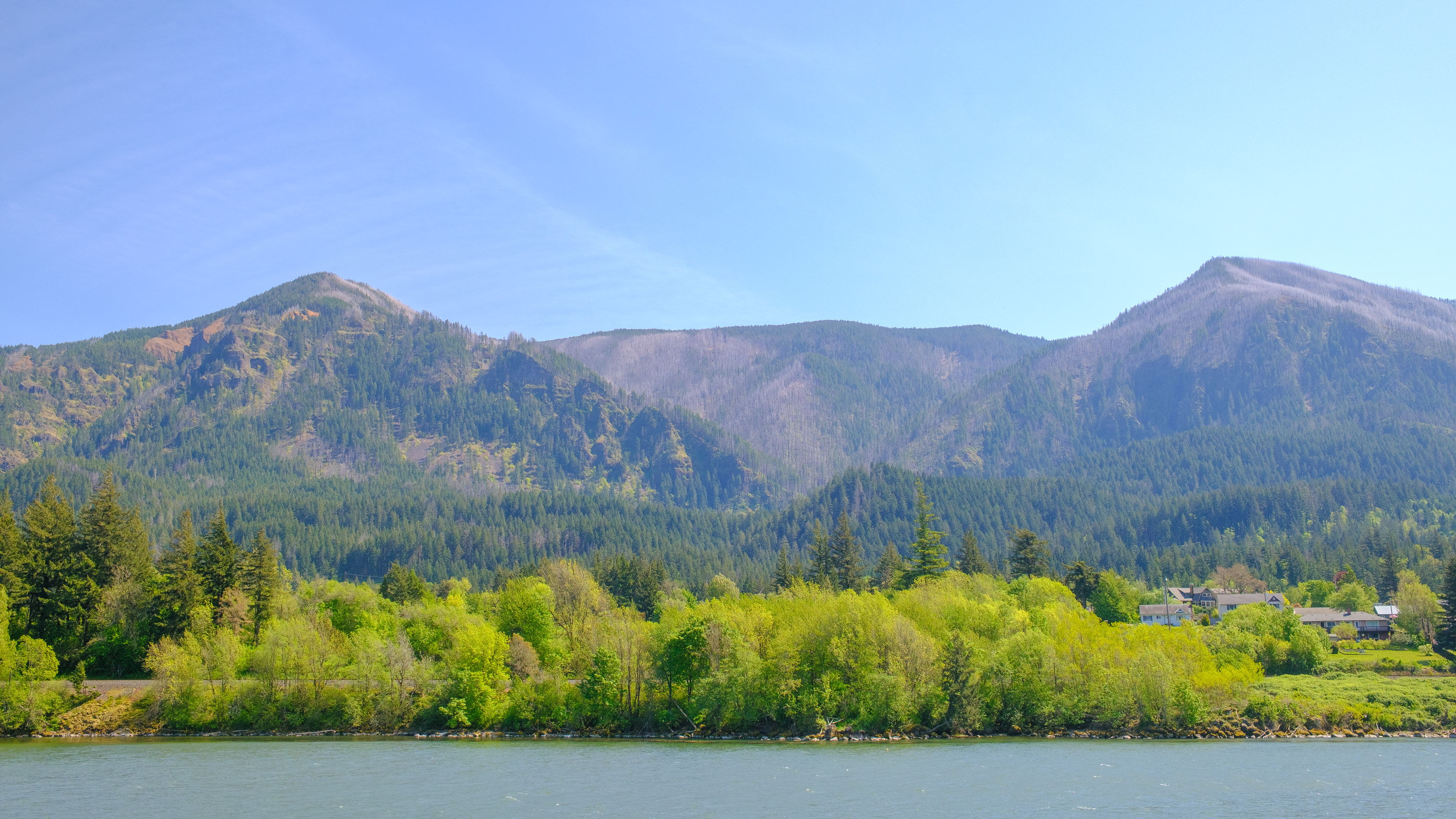 Scenic view of the Columbia River Gorge with water in the foreground and jagged mountains in the background with a bright blue sky