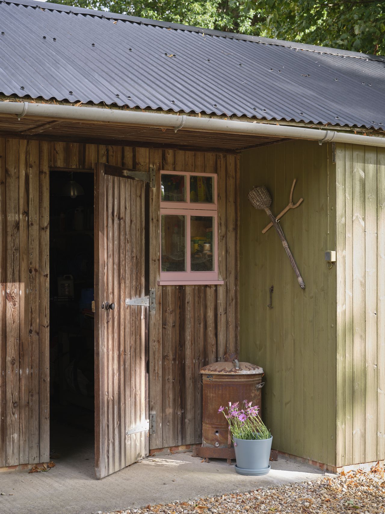 An outdoor shed that is part natural wood, part wood painted in a light olive green. The window on the shed is painted light pink.